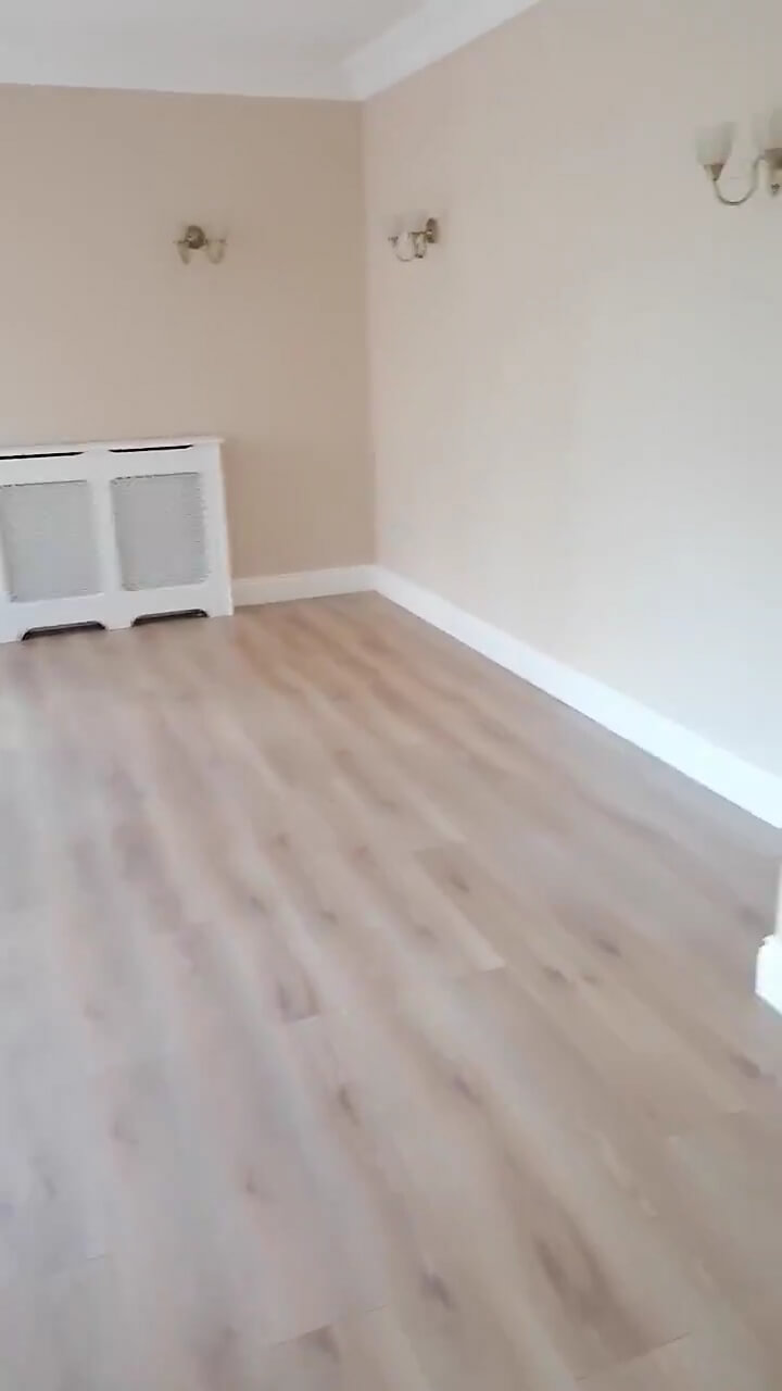 a portion of a living room with magnolia walls, light brown laminate flooring and wall lights. A white radiator cover is on the back wall